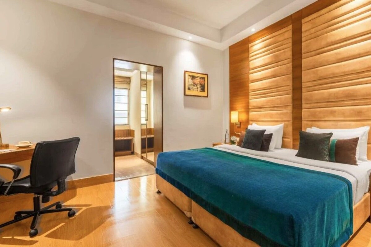 A hotel room with a bed, bedside table, lamp, and a desk with a chair.