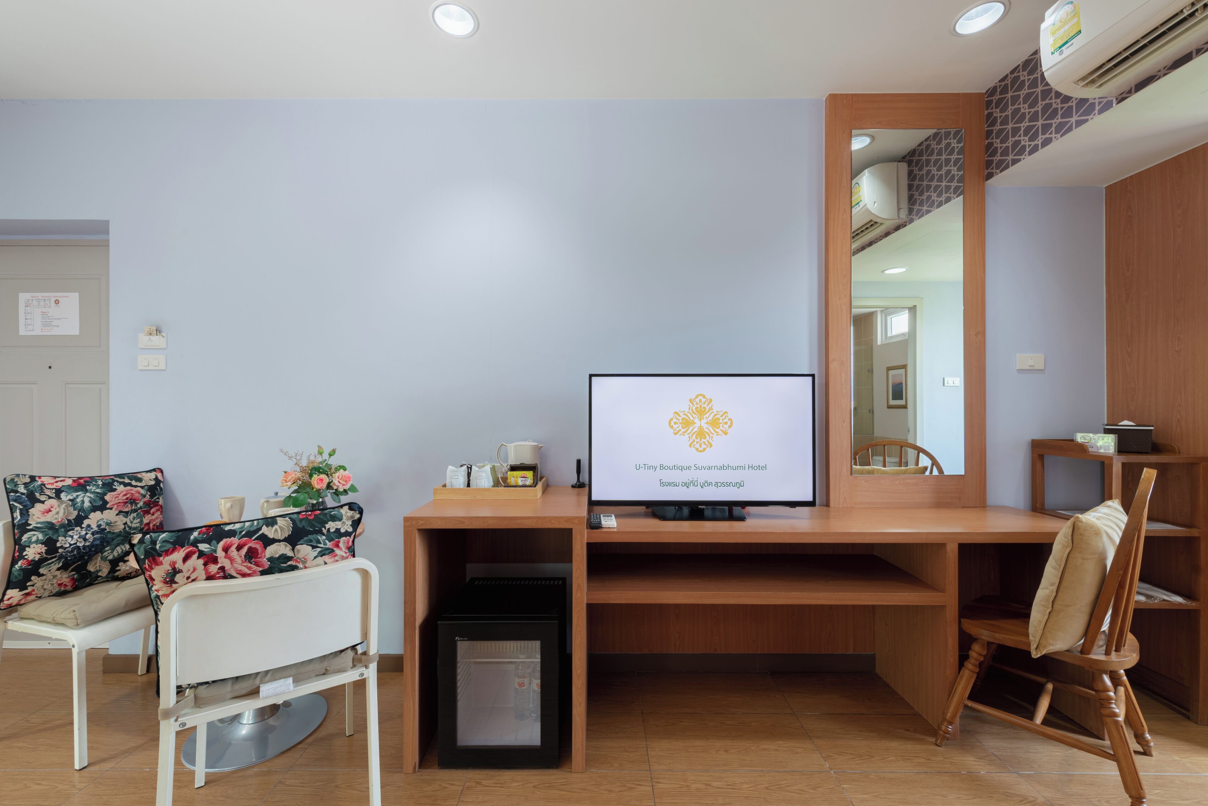 A hotel room with a bed, a desk with a computer, a chair, a small fridge, and a TV displaying a hotel logo.