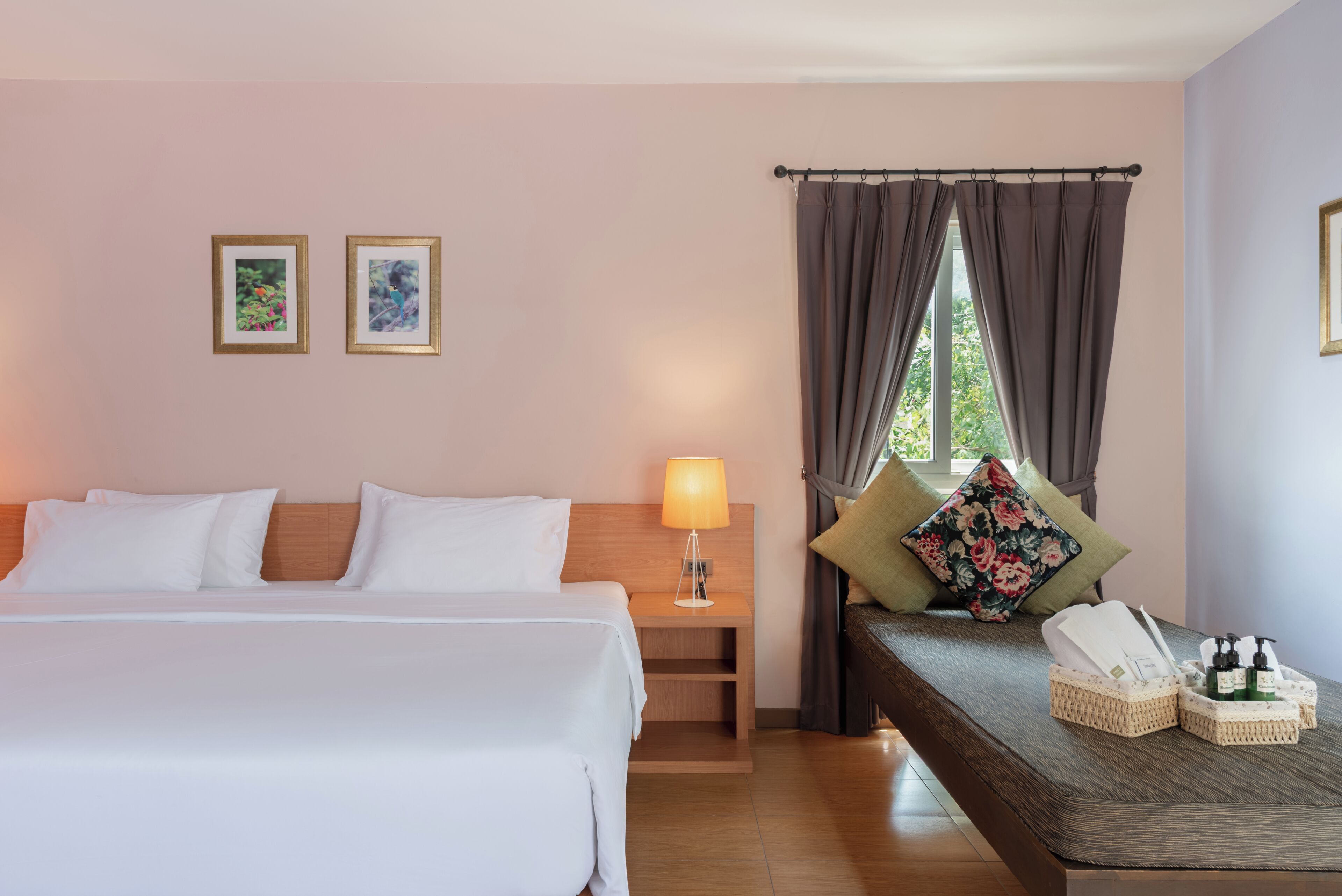 Una habitación de hotel con cama, mesita de noche, lámpara y un sofá con un cojín estampado con motivos florales.