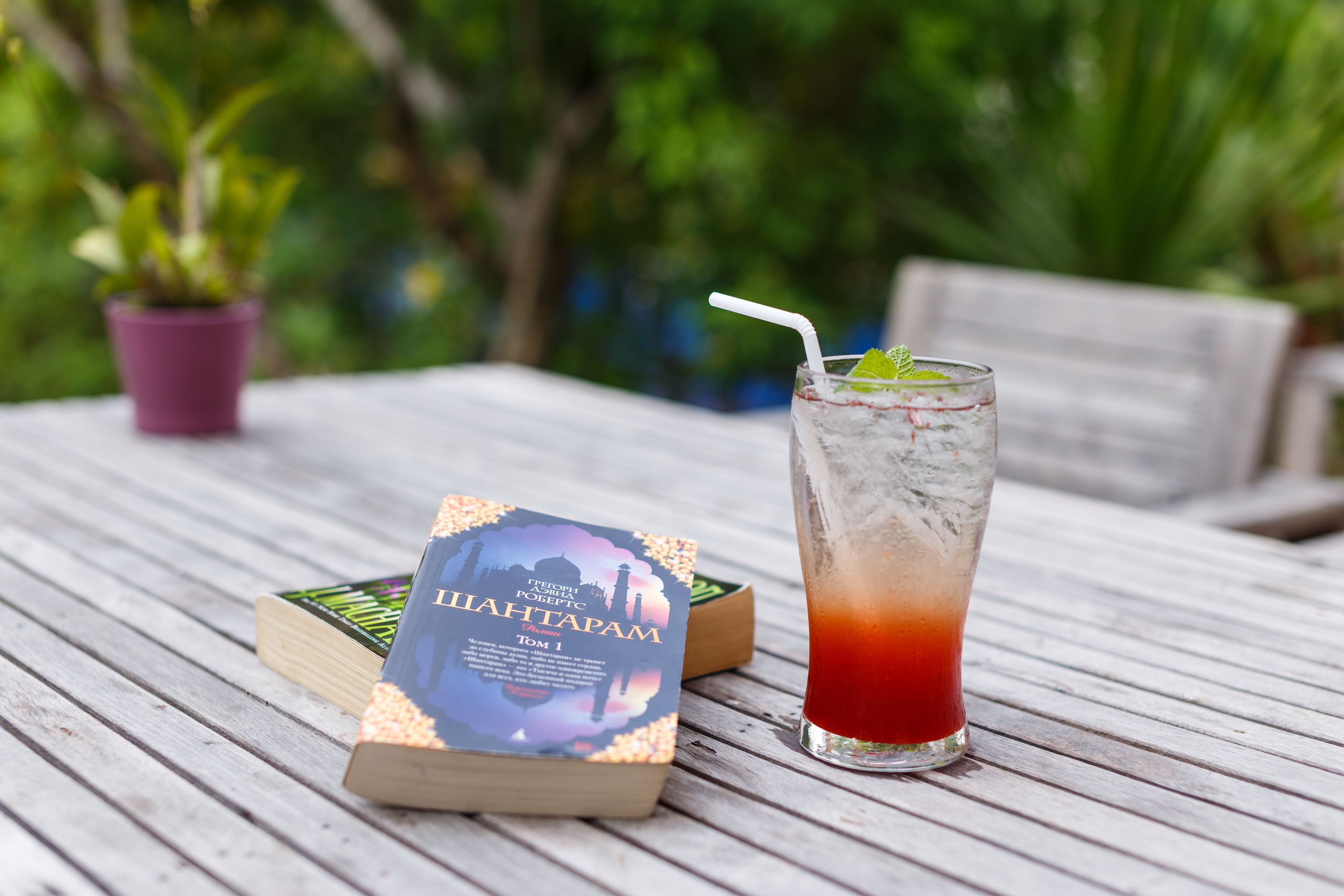 A book titled "Lilahtapam" and a glass of iced drink with a straw on a wooden table.