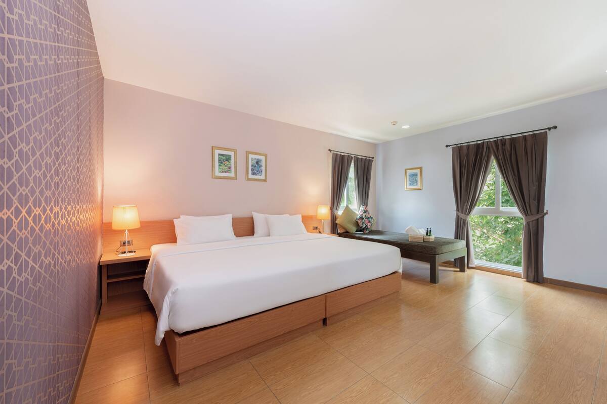 A hotel room with a large bed, bedside tables, a desk, and a view of greenery through the window.
