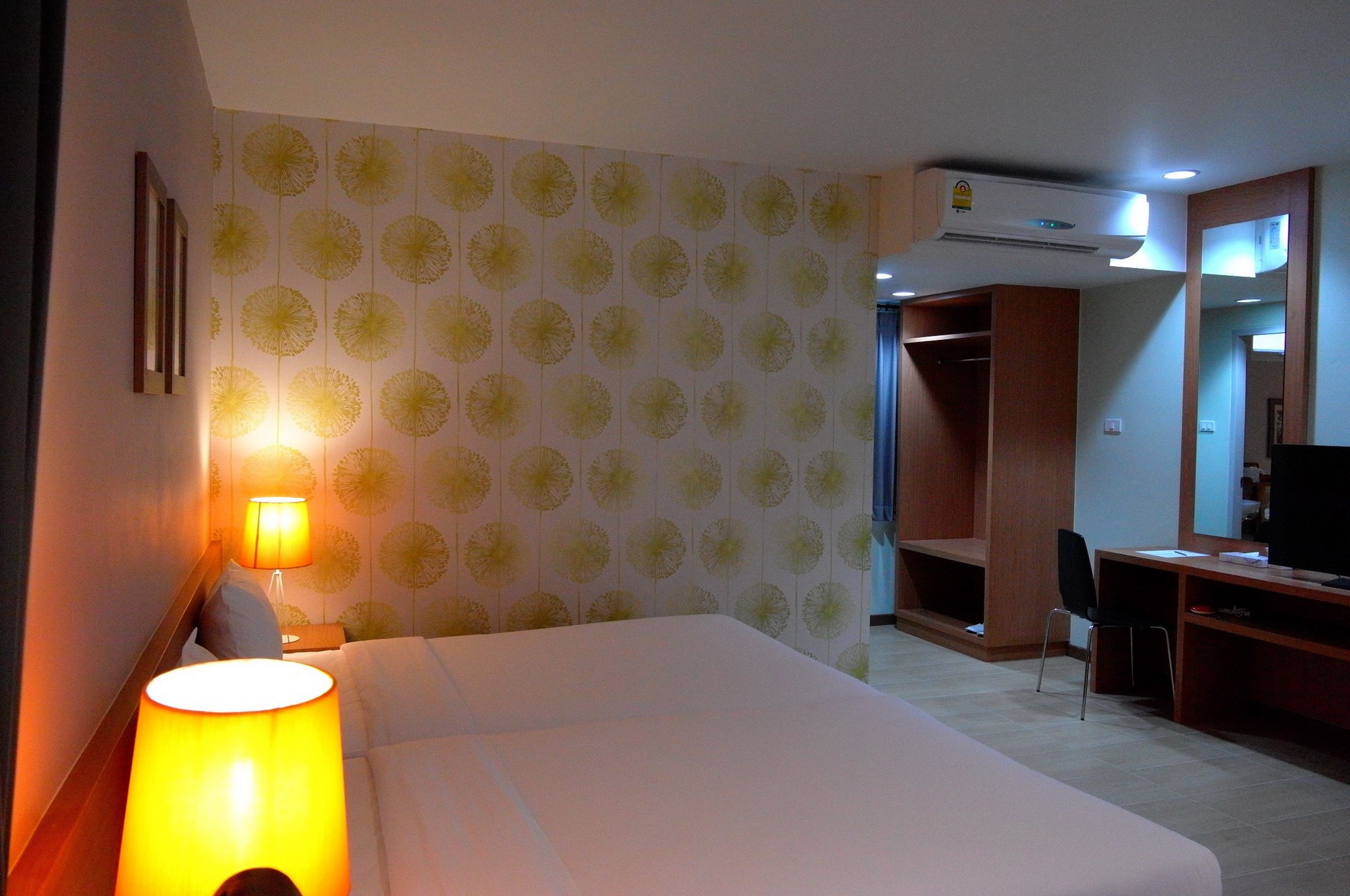 A hotel room with a bed, a desk, a chair, an air conditioning unit, and a wardrobe.