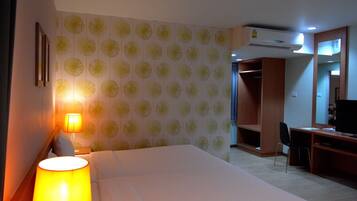 A hotel room with a bed, a desk, a chair, an air conditioning unit, and a wardrobe.