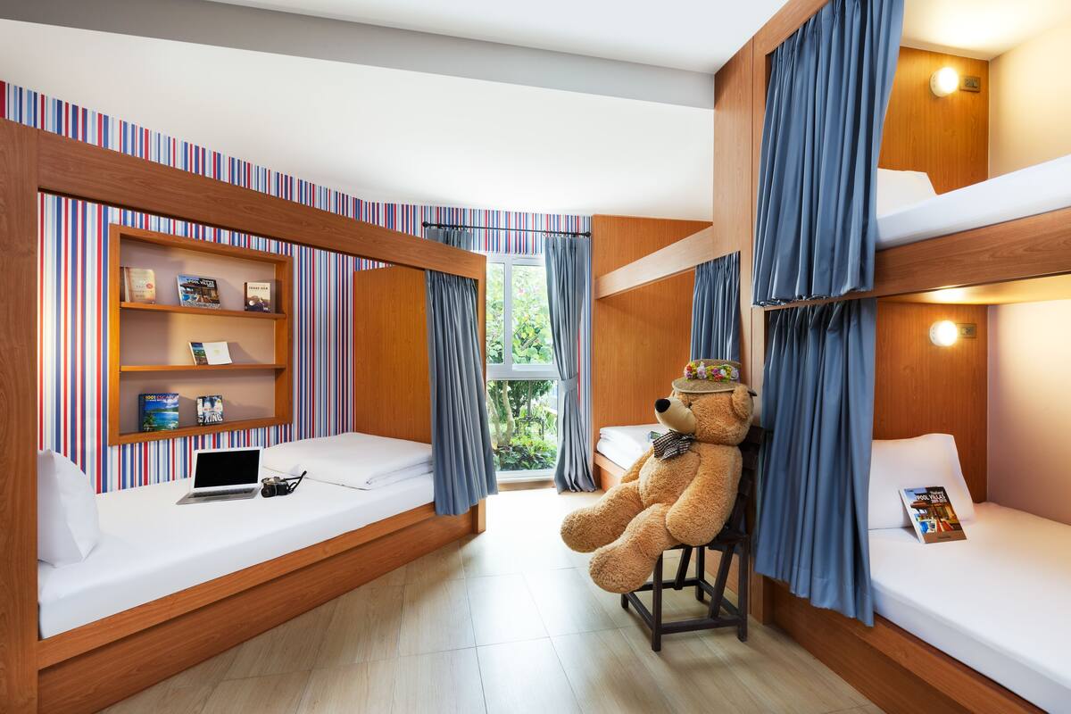 A bunk bed room with a teddy bear on the lower bunk, a laptop on the bed, and a bookshelf with books and a toy.