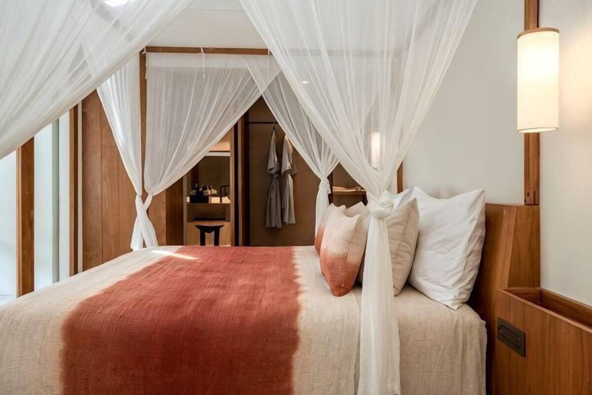 A bed with a canopy, a bedside table, and a wall-mounted light fixture.