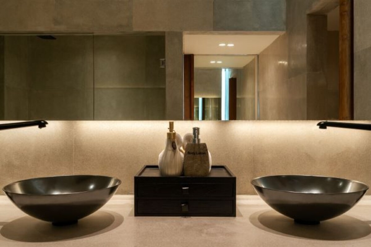 A modern bathroom with two large black bowls on a countertop, a dark wooden box with bottles, and a large mirror above.