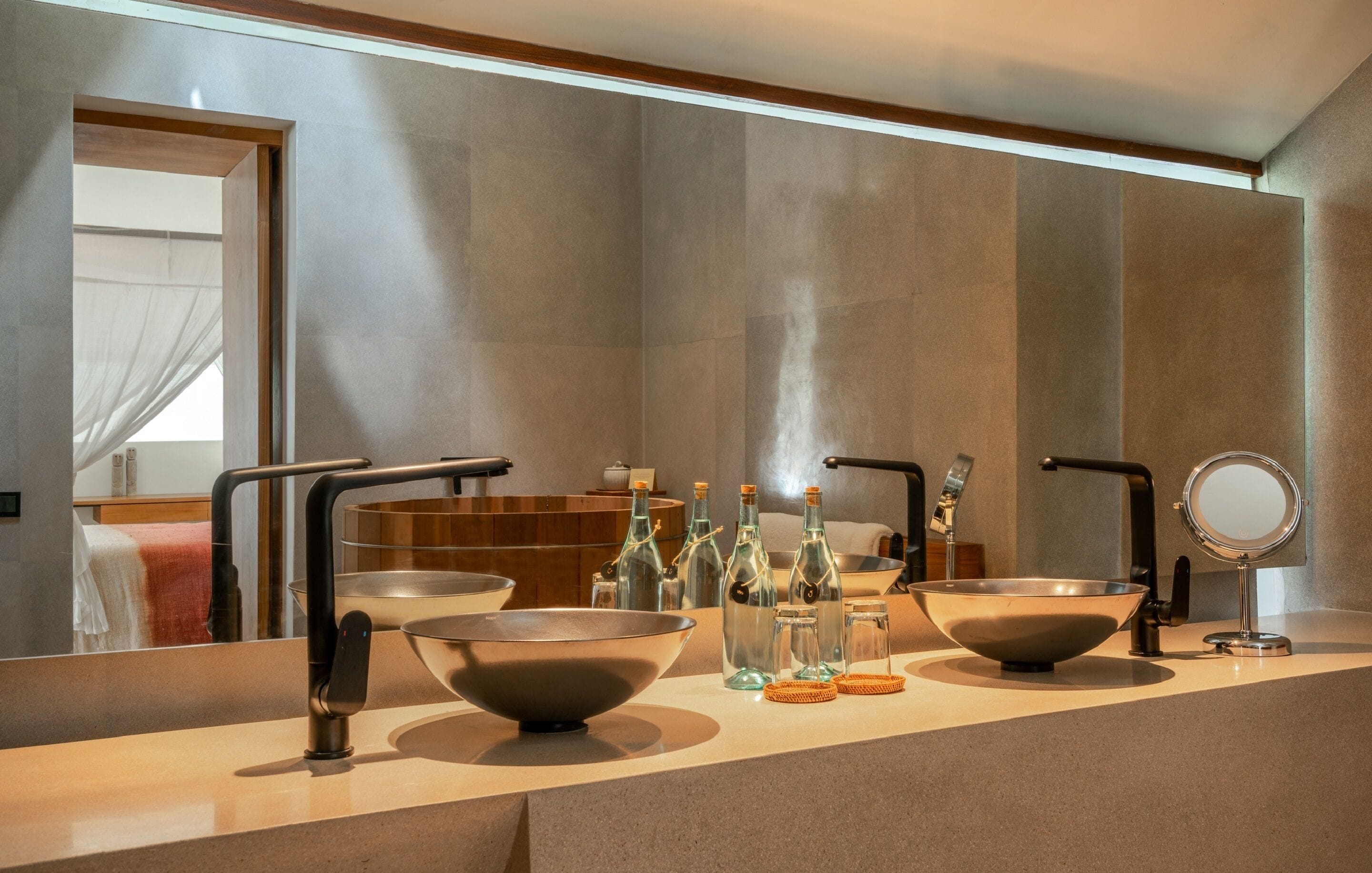 Un baño moderno con un espejo grande, dos lavamanos y un lavabo espacioso. Se observan botellas y un perchero para toallas.
