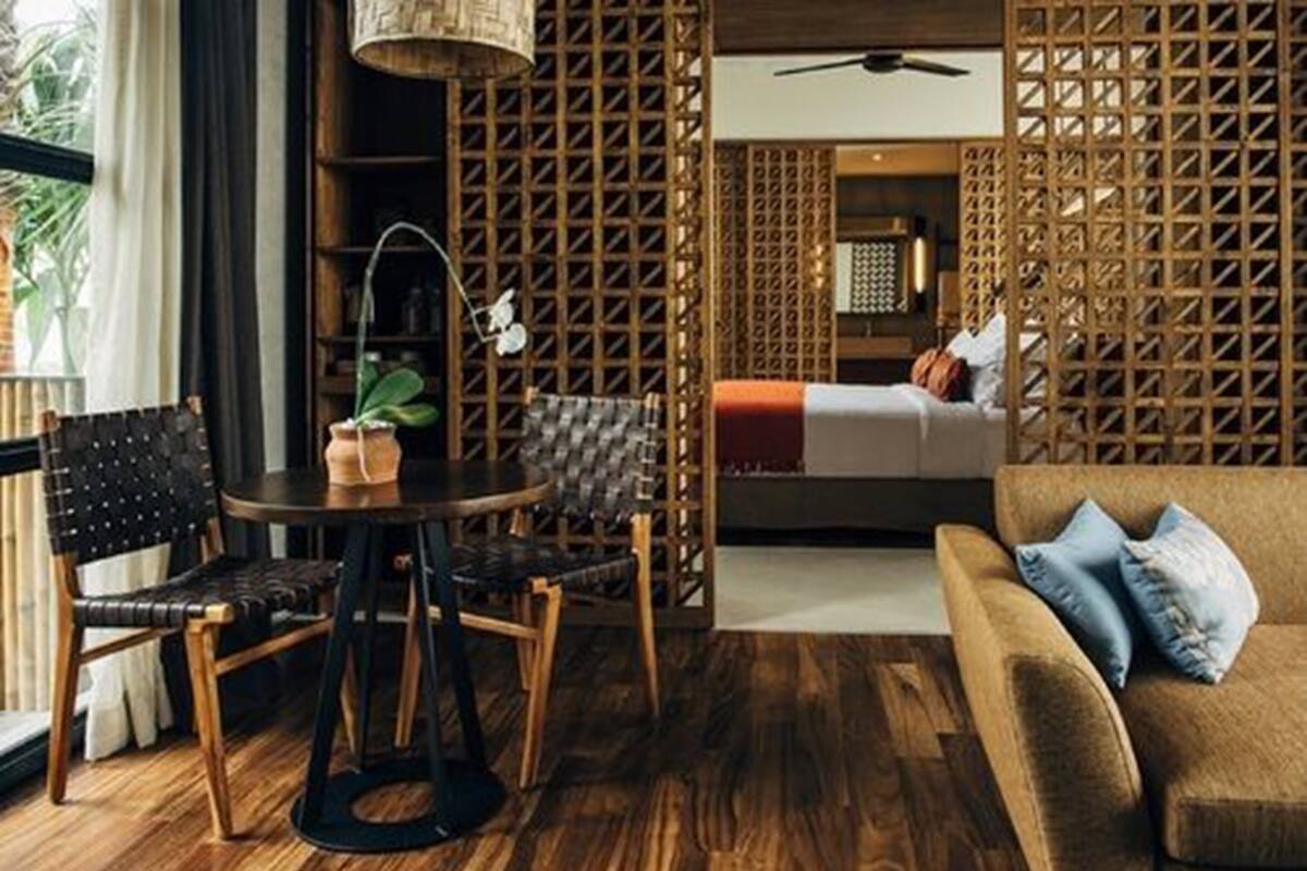 A room with a wooden floor, a round table with chairs, a sofa, and a bed with a person in it.