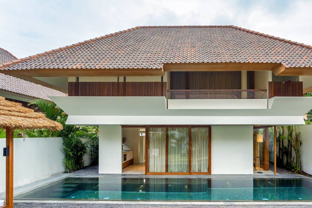 A modern two-story house with a tiled roof, a swimming pool, and a well-maintained garden.