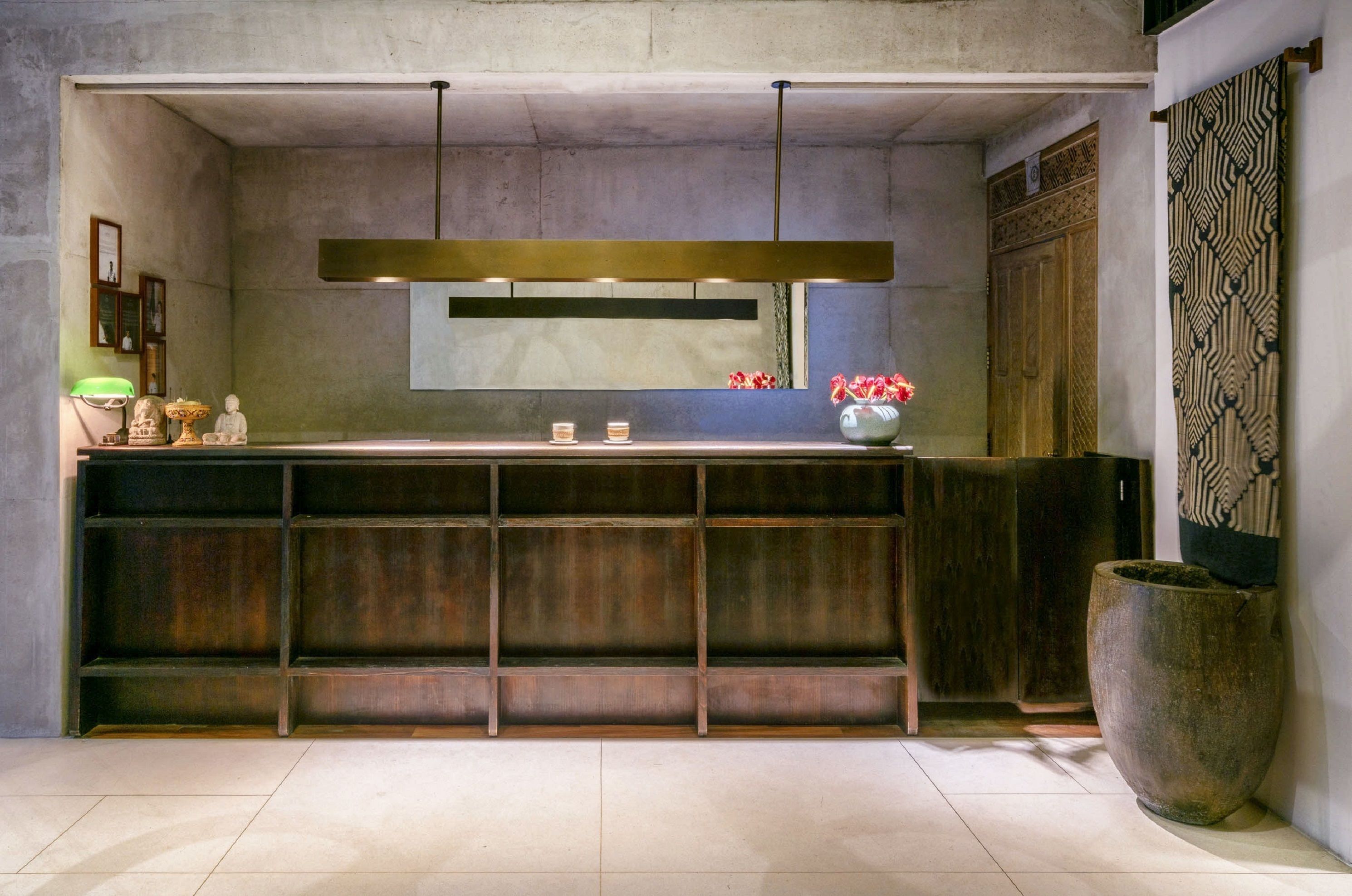 A reception area with a wooden reception desk, a large vase with flowers, and a patterned wall hanging.