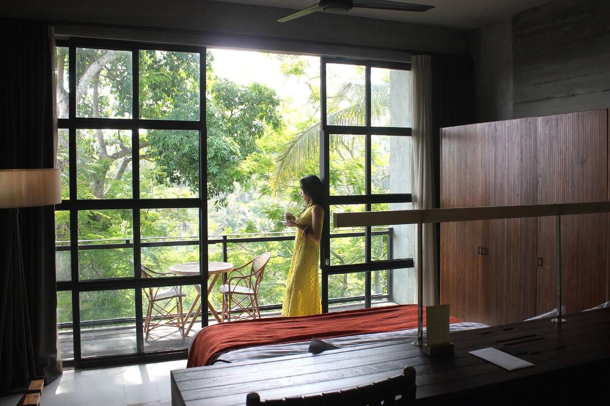 A room with large windows, a bed, a chair, and a table.
