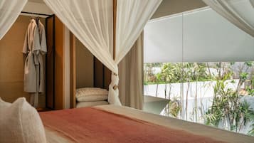A bedroom with a bed, a hanging robe, and a view of greenery outside.