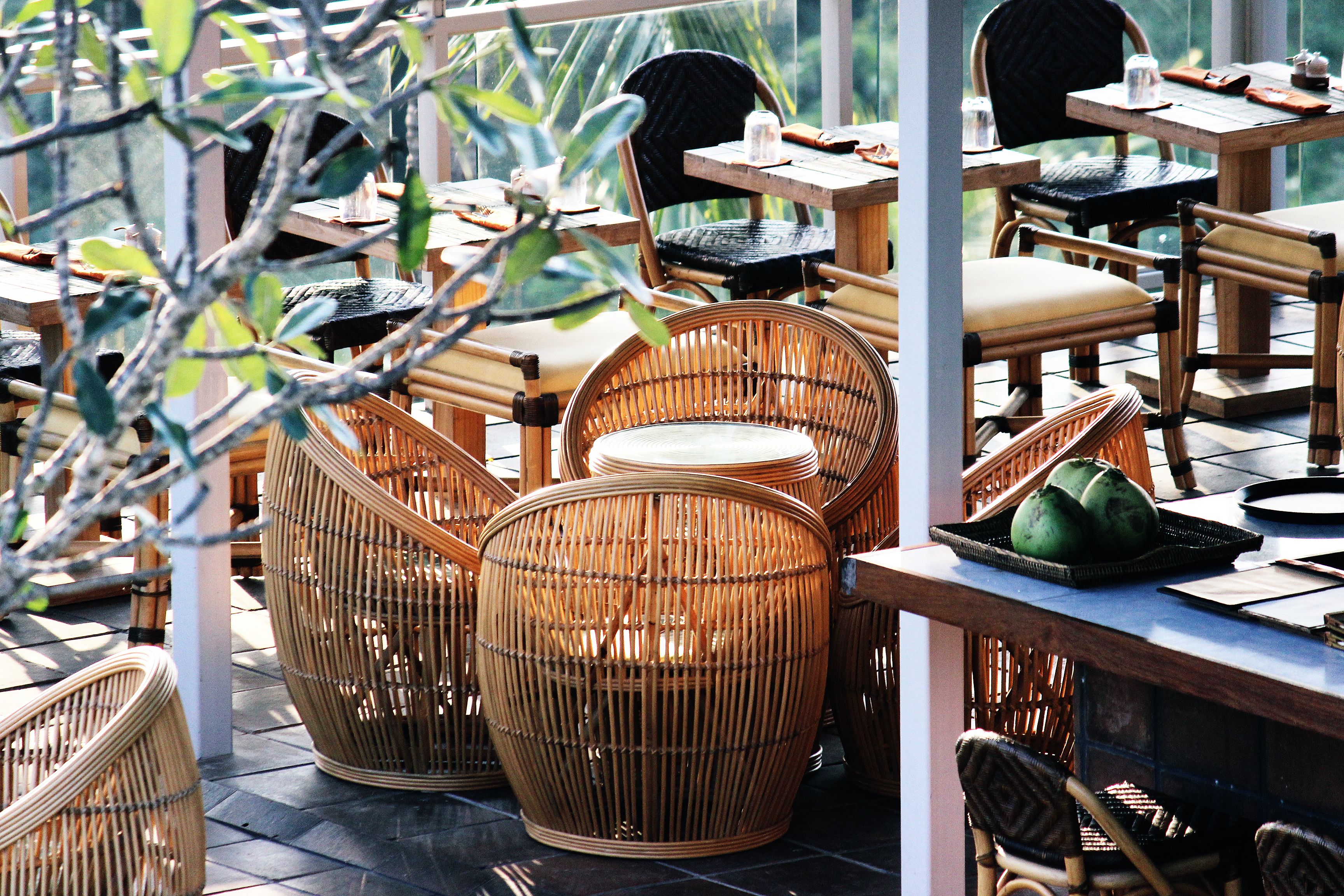 A restaurant with wicker furniture, including chairs and tables, and a view of greenery outside.