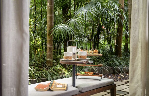 Une table sur laquelle sont disposés un plateau de nourriture et des boissons, le tout mis en valeur par un décor de verdure luxuriante.