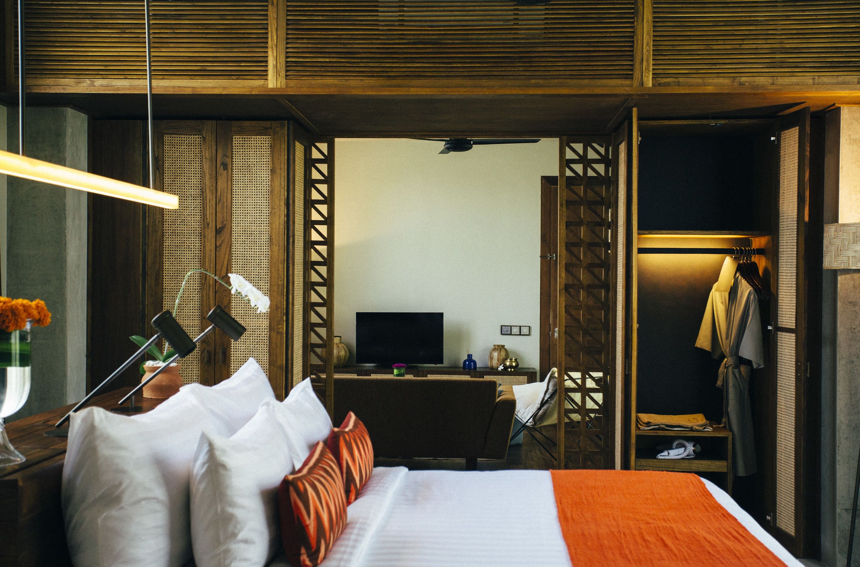 Una habitación de hotel con cama, mesita de noche, lámpara, televisor y armario.