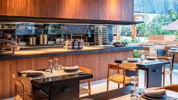 Un restaurante moderno con interior de madera, una zona de bar con equipo de cocina y mesas al aire libre con vistas a zonas verdes.