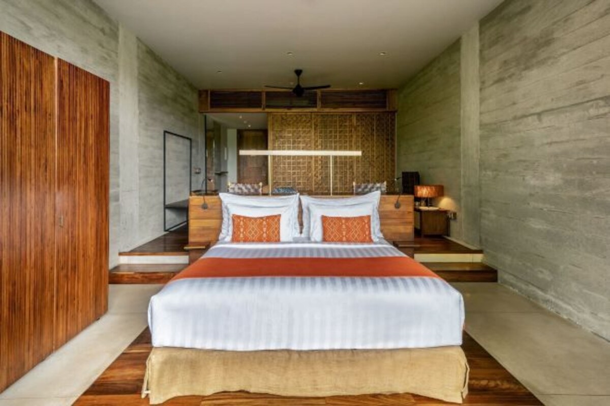 A modern bedroom with a large bed, wooden paneling on the walls, a ceiling fan, and a nightstand with a lamp.