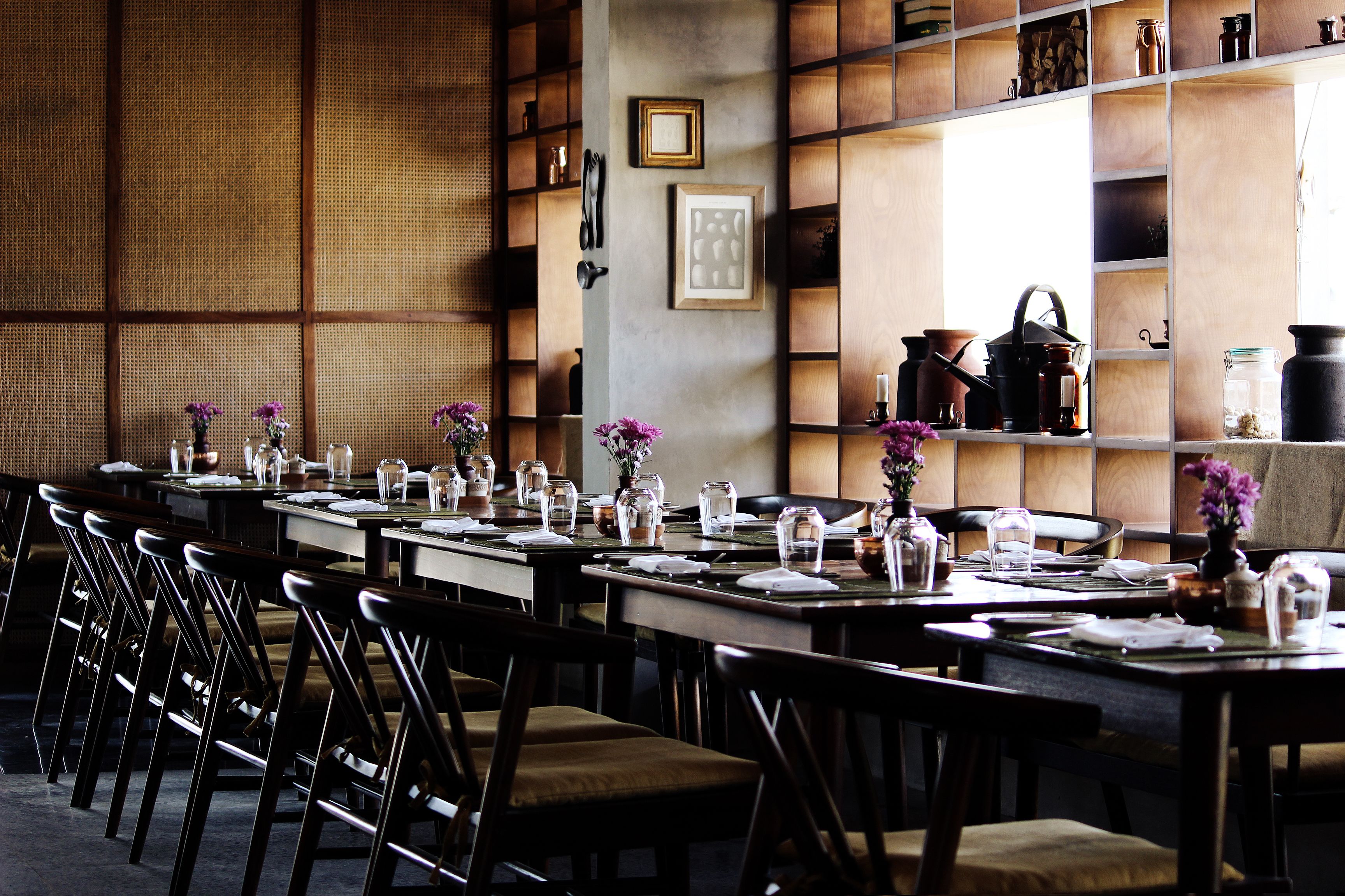 A restaurant with long tables, chairs, and shelves with kitchen items.