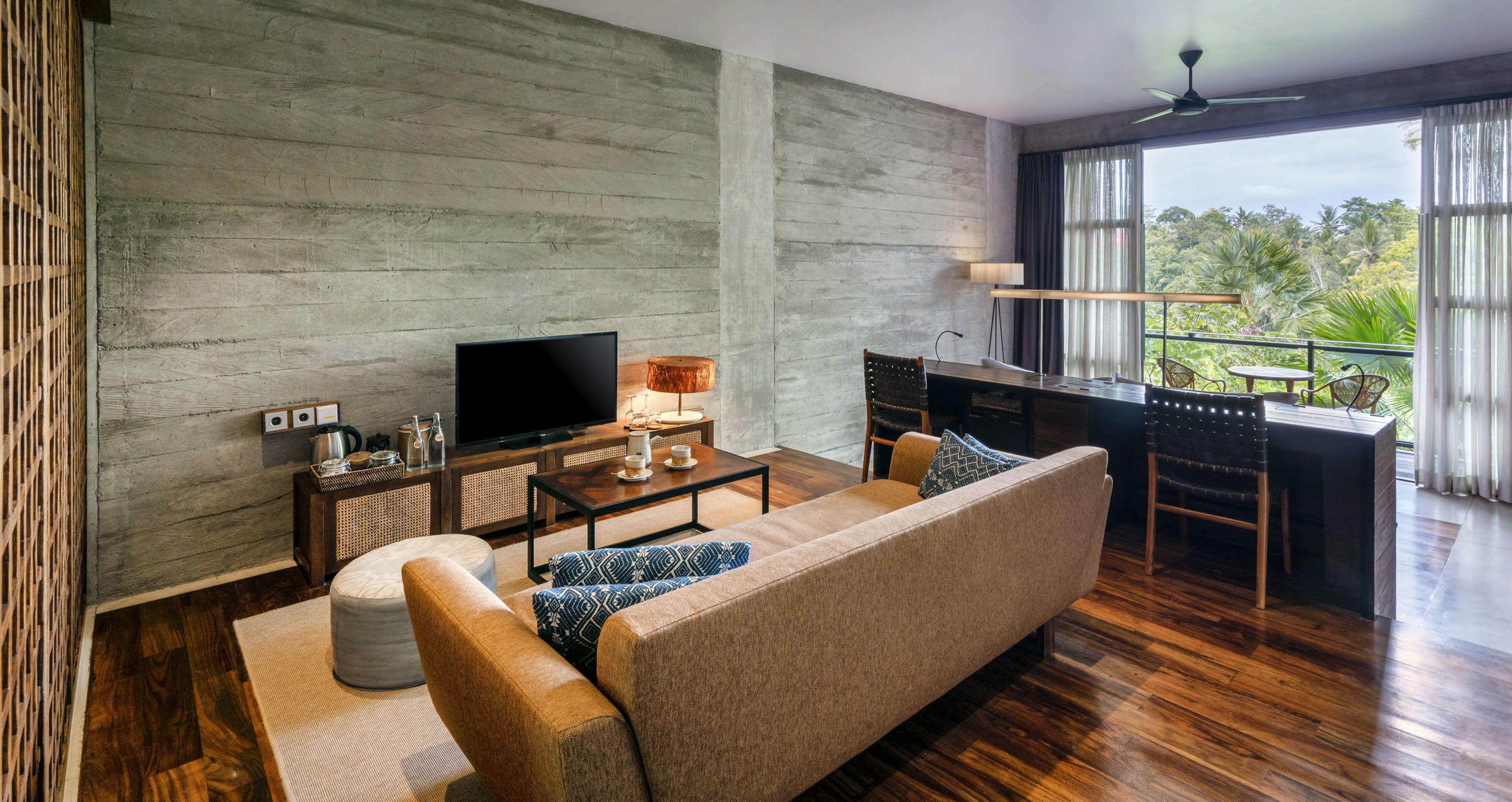 A modern living room with a sofa, coffee table, TV, and a balcony with a view of greenery.