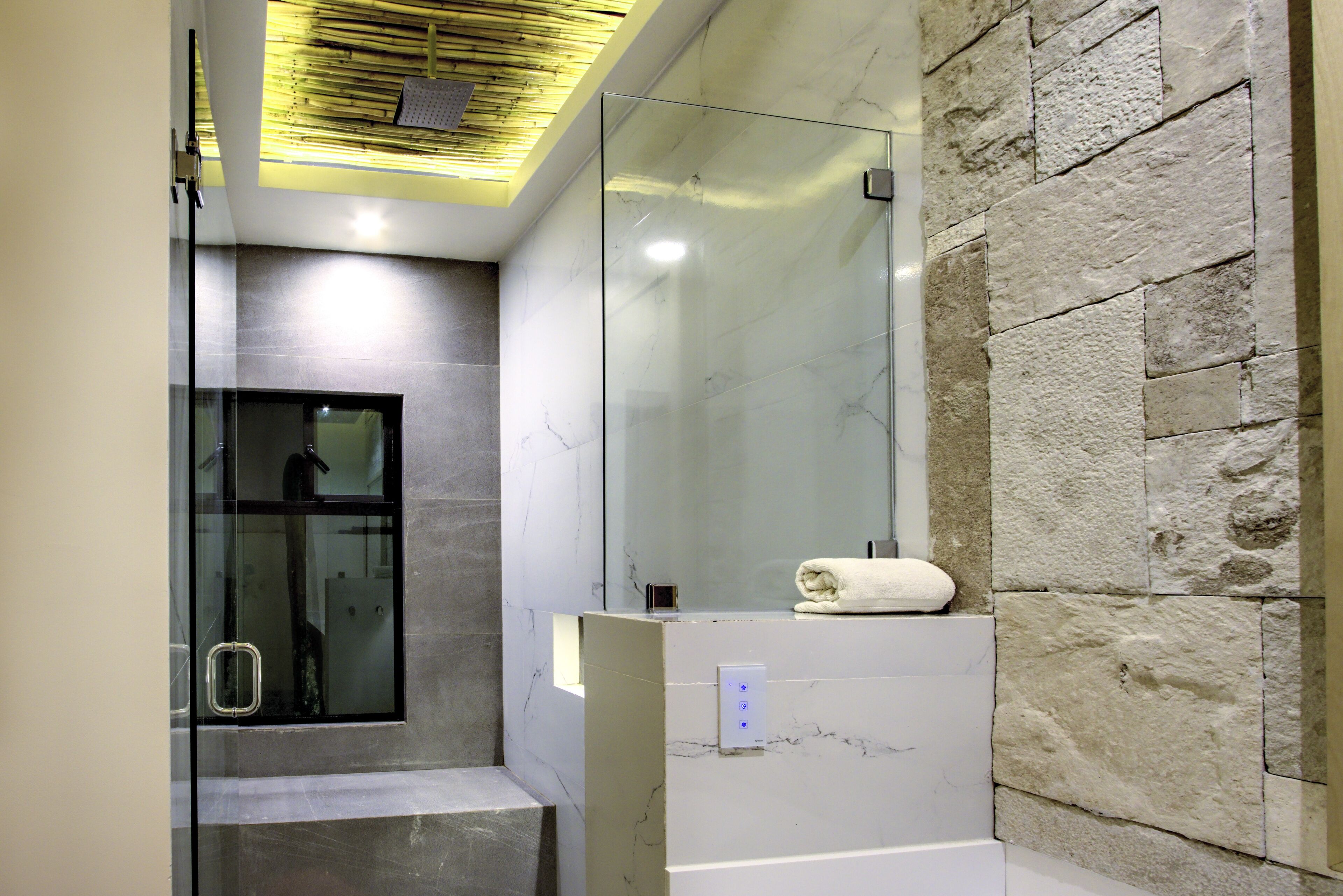 Un baño moderno con cabina de ducha de vidrio, encimera de mármol y pared de piedra.