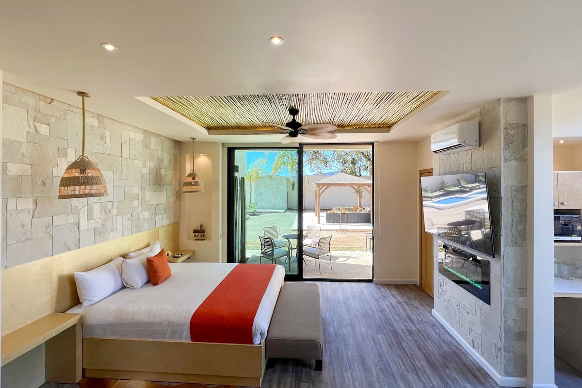Une chambre à coucher moderne avec un grand lit, un ventilateur de plafond et un téléviseur fixé au mur.