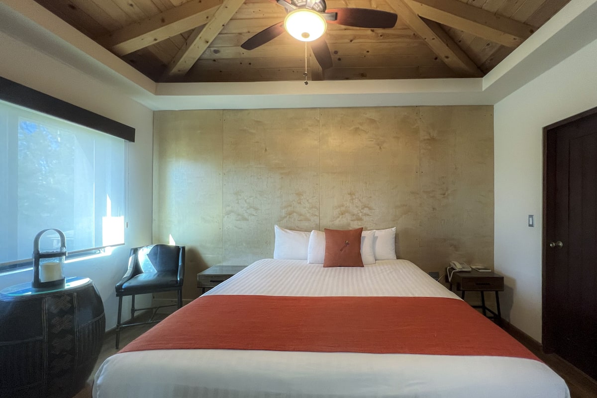 Une chambre avec un grand lit, un ventilateur de plafond, une fenêtre et une chaise.