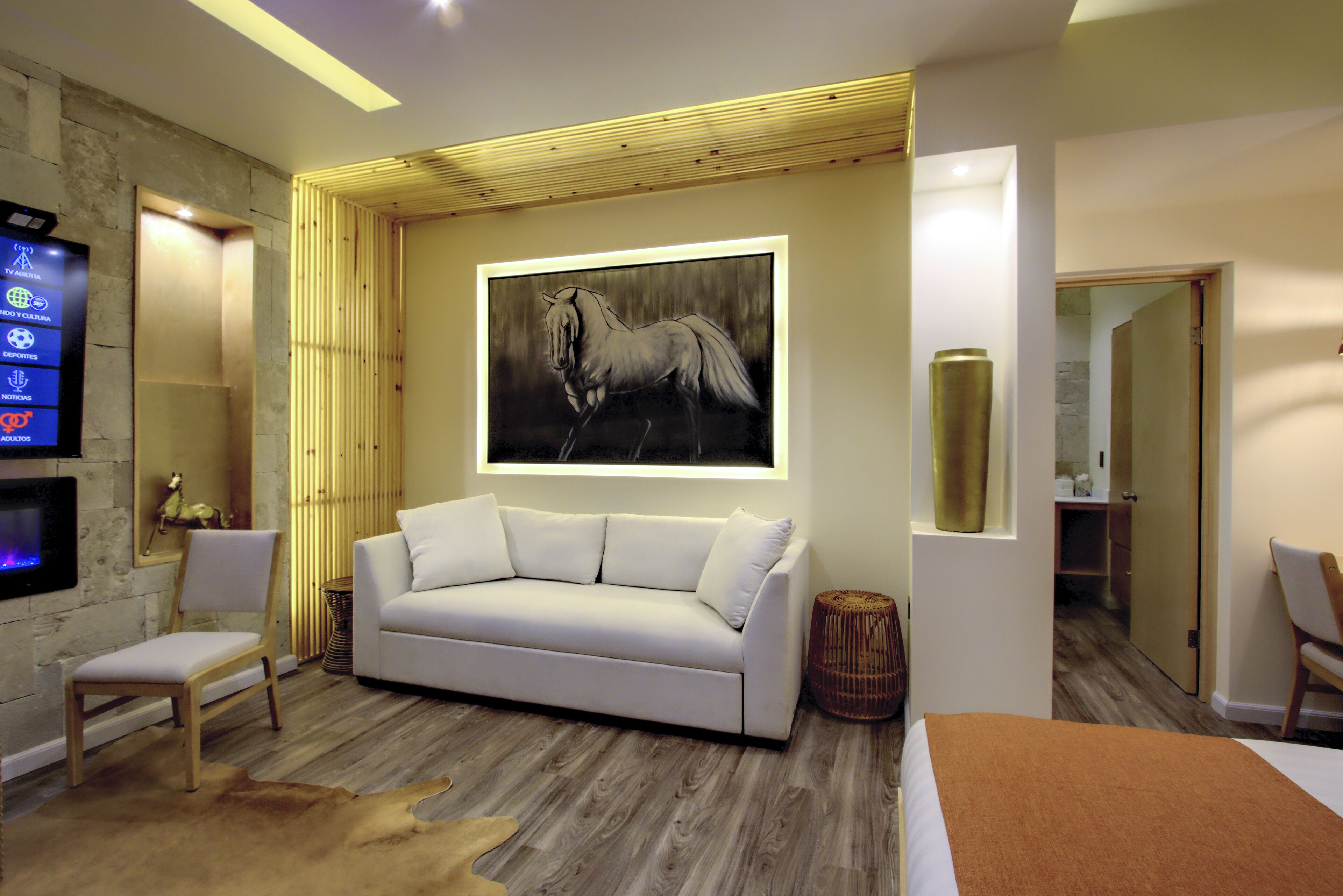 A modern hotel room with a white sofa, a mounted TV, a large framed horse painting, and a wooden floor.