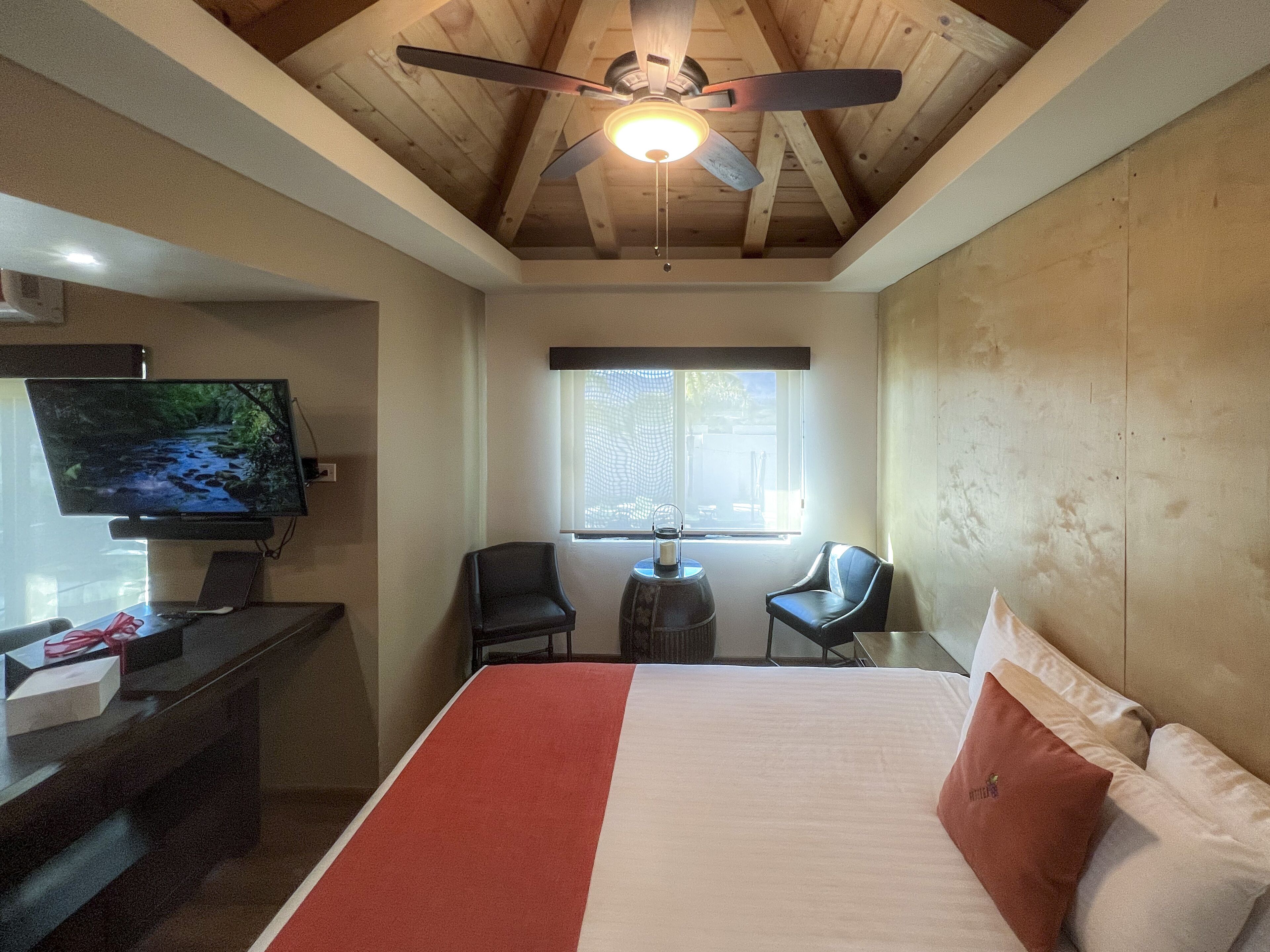 A bedroom with a bed, a desk, a television, and a ceiling fan.