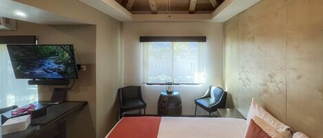 A bedroom with a bed, a desk, a television, and a ceiling fan.