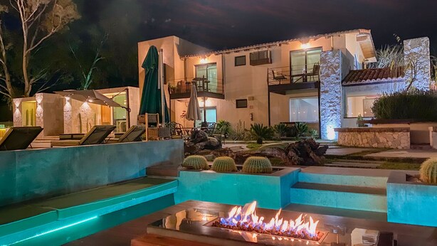A modern outdoor pool area with a fire feature, lounge chairs, and a well-lit building with multiple levels and balconies. - Bottega Hotel Boutique (Valle de Guadalupe)