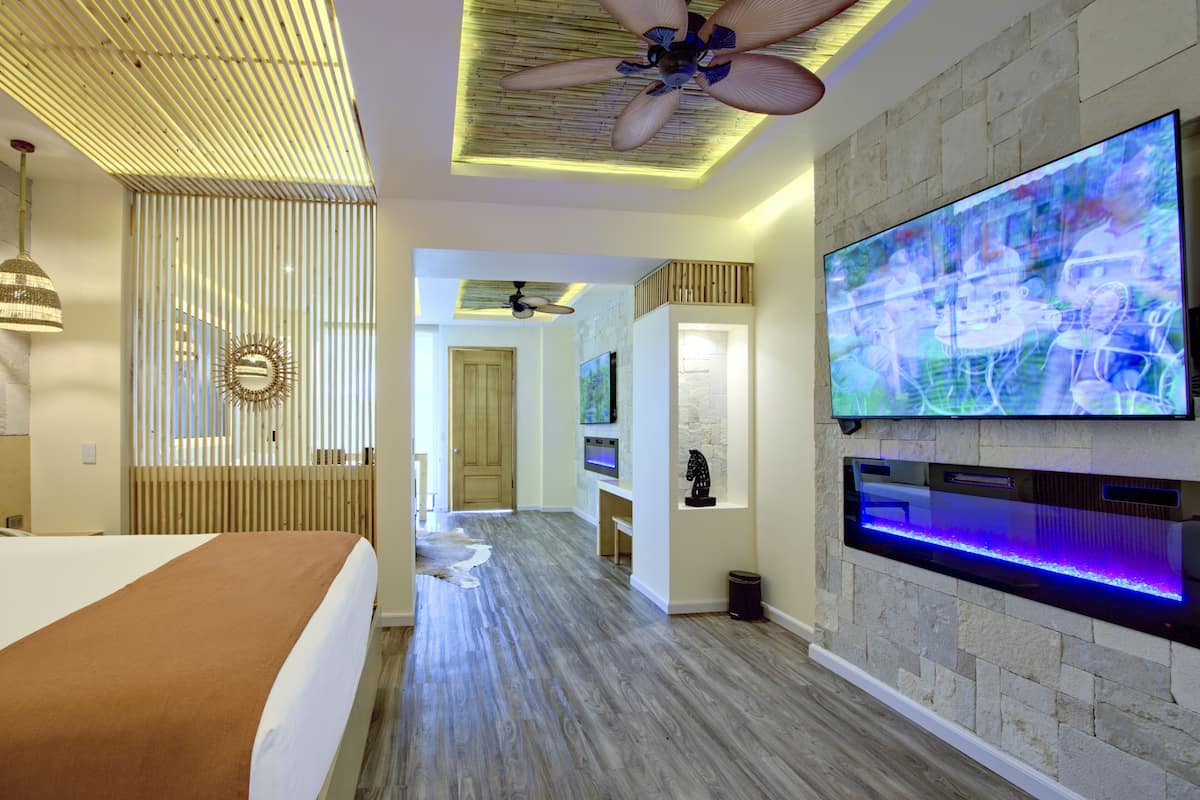 Une chambre d’hôtel moderne dotée d’un grand téléviseur à écran plat, d’un ventilateur de plafond et d’un plancher en bois.