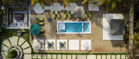 Vista aérea de un hotel con piscina central identificada como “Bottega by Hotel Boutique”, rodeada de áreas de estar al aire libre y palmeras.