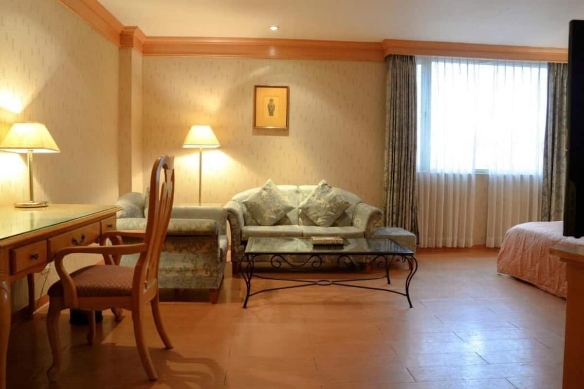 Et hotelværelse med skrivebord i træ, to stole, en sofa, et lille bord og en seng.
