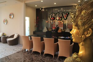 Un hall con sillas de mimbre, un mostrador de recepción y un busto dorado decorativo.