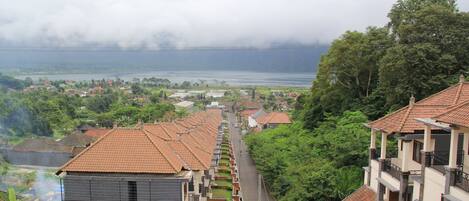 A row of residential buildings with red-tiled roofs, a narrow street, and a view of a lake with surrounding greenery.