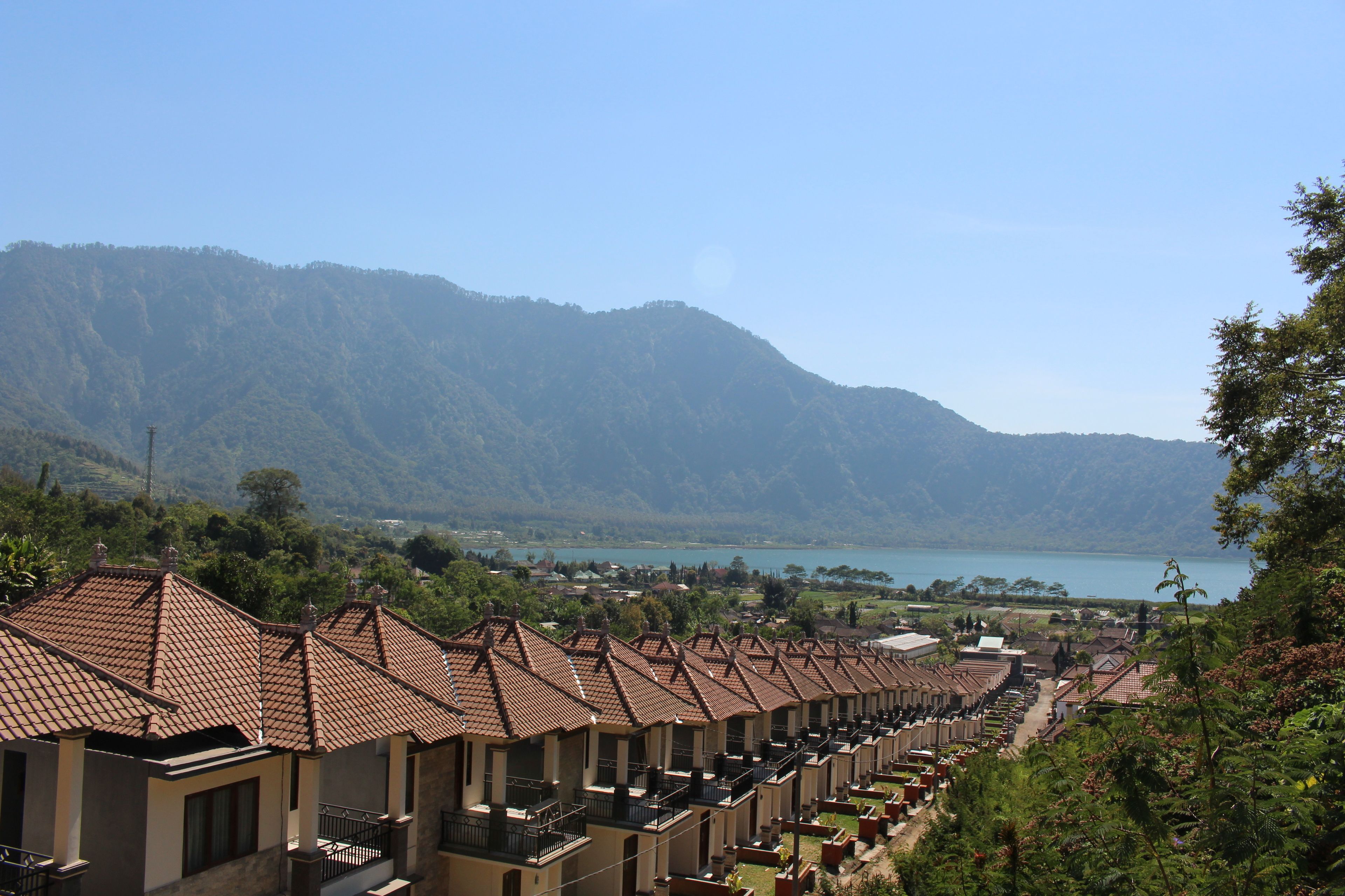 A row of traditional-style buildings with tiled roofs, likely a hotel or resort, overlooking a lake and mountains.