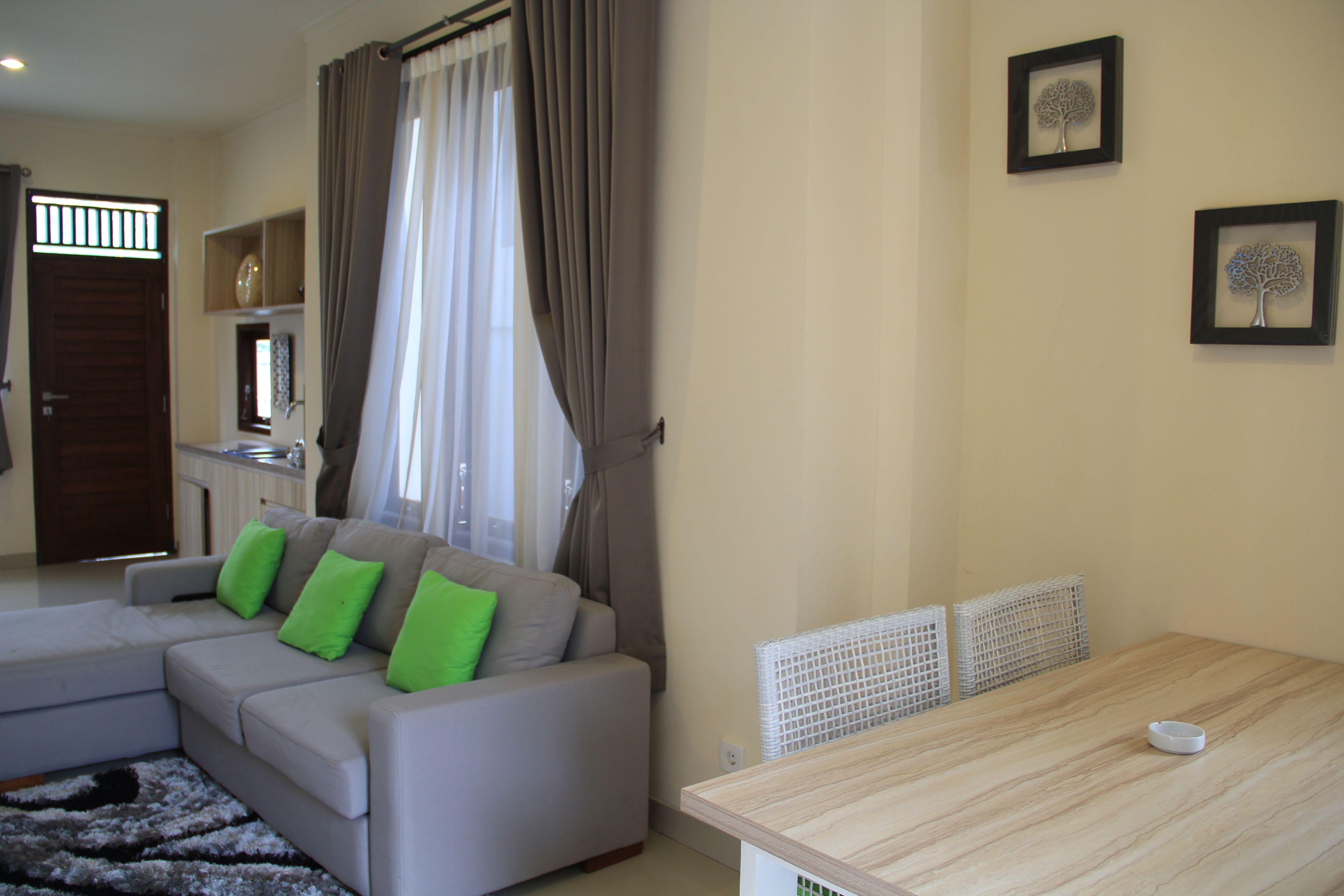 A modern living room with a grey sofa, green cushions, a wooden dining table, and a kitchen area in the background.