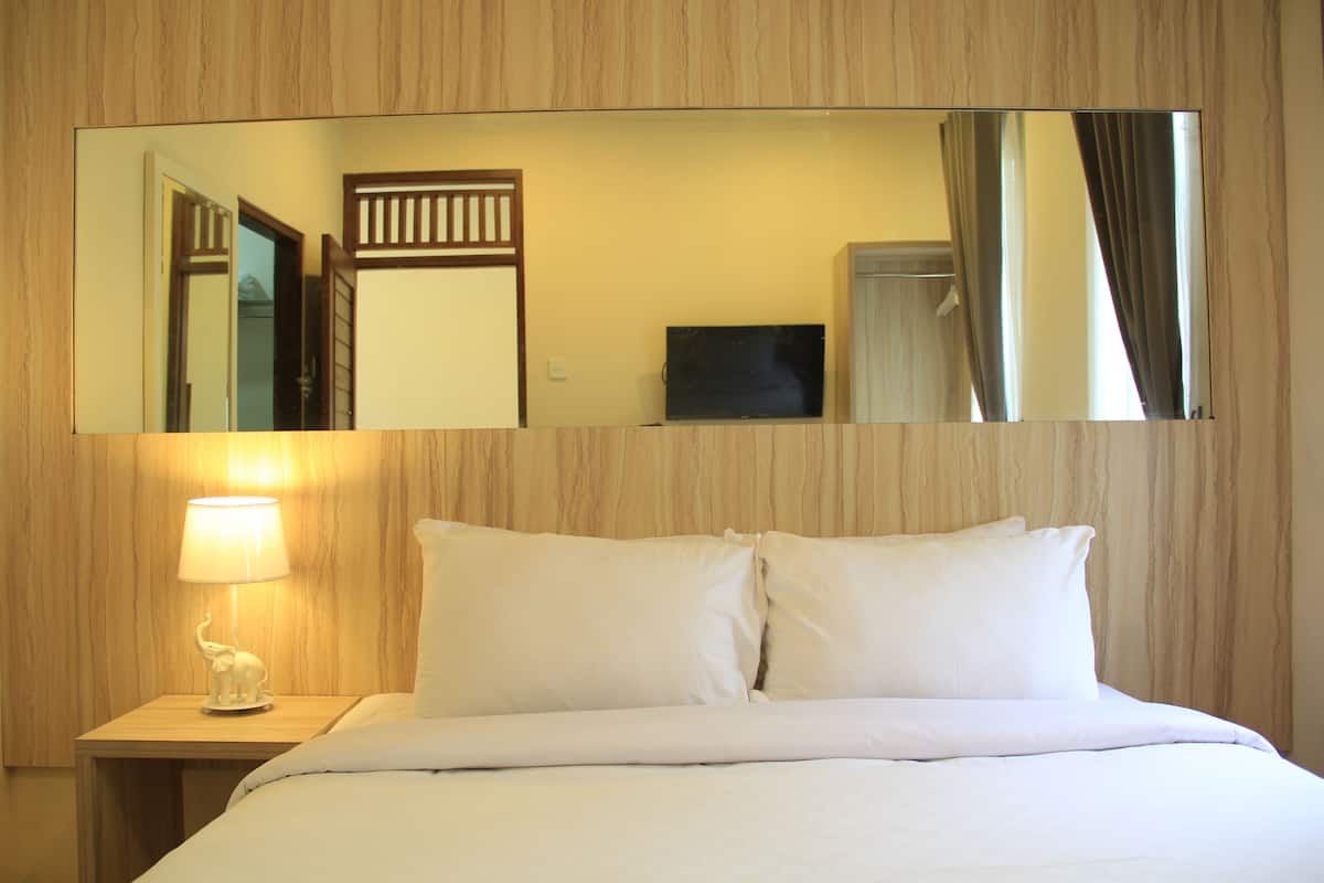 A hotel room with a bed, a nightstand with a lamp, and a large mirror on the wall.