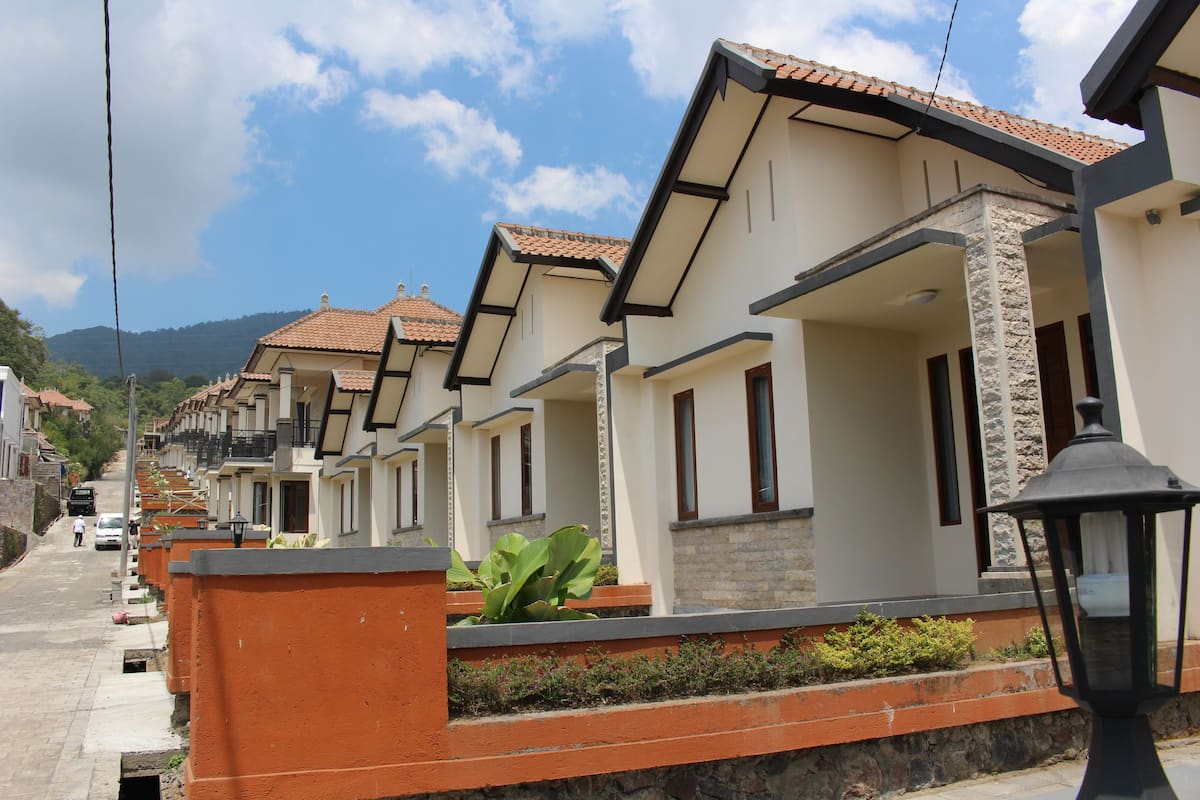 A row of modern, two-story houses with tiled roofs and stone accents, along a paved street with a clear sky.
