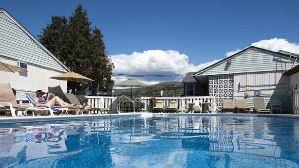 A swimming pool with lounge chairs and umbrellas, surrounded by buildings with a view of hills. - Valley Star Motel (Penticton)