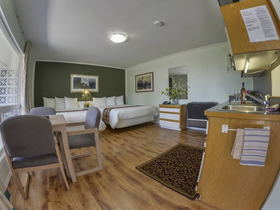 Una habitación con cama, escritorio, silla, una kitchenette pequeña y ventana con vistas.