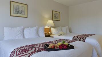 Hotelkamer met twee bedden, witte lakens, een dienblad met croissants, aardbeien en sap, een bedlamp en twee florale schilderijen in lijsten aan de muur.