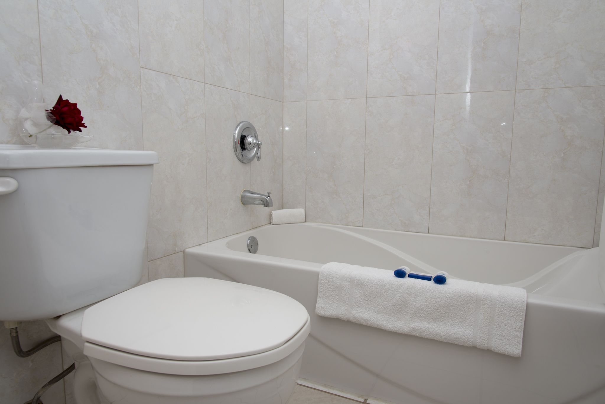 Un baño con inodoro, bañera y pared de azulejos blancos.