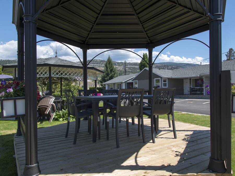 Un patio exterior techado con una mesa y sillas, rodeado por una terraza de madera.