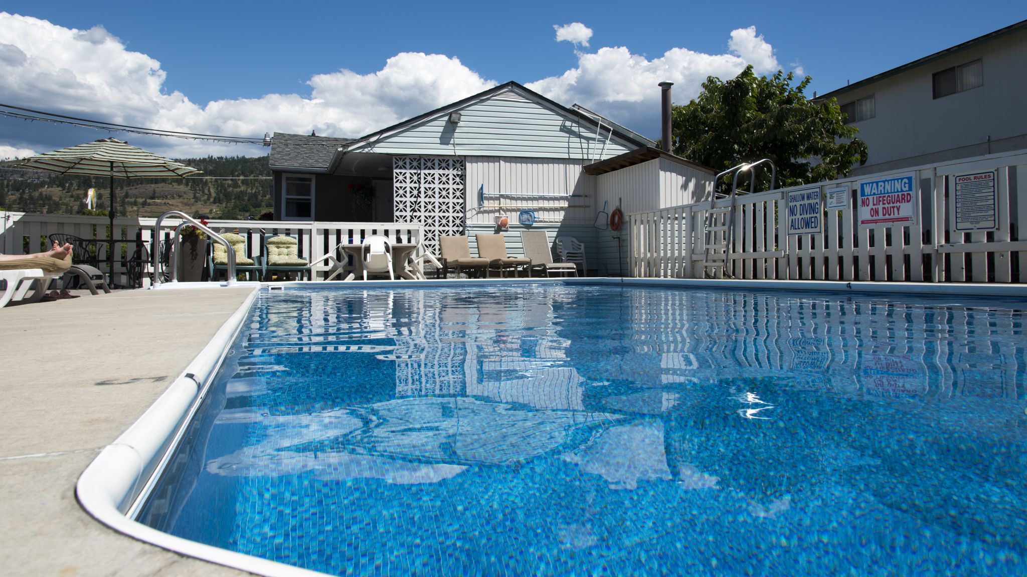 A swimming pool with a white fence, lounge chairs, and a building in the background.