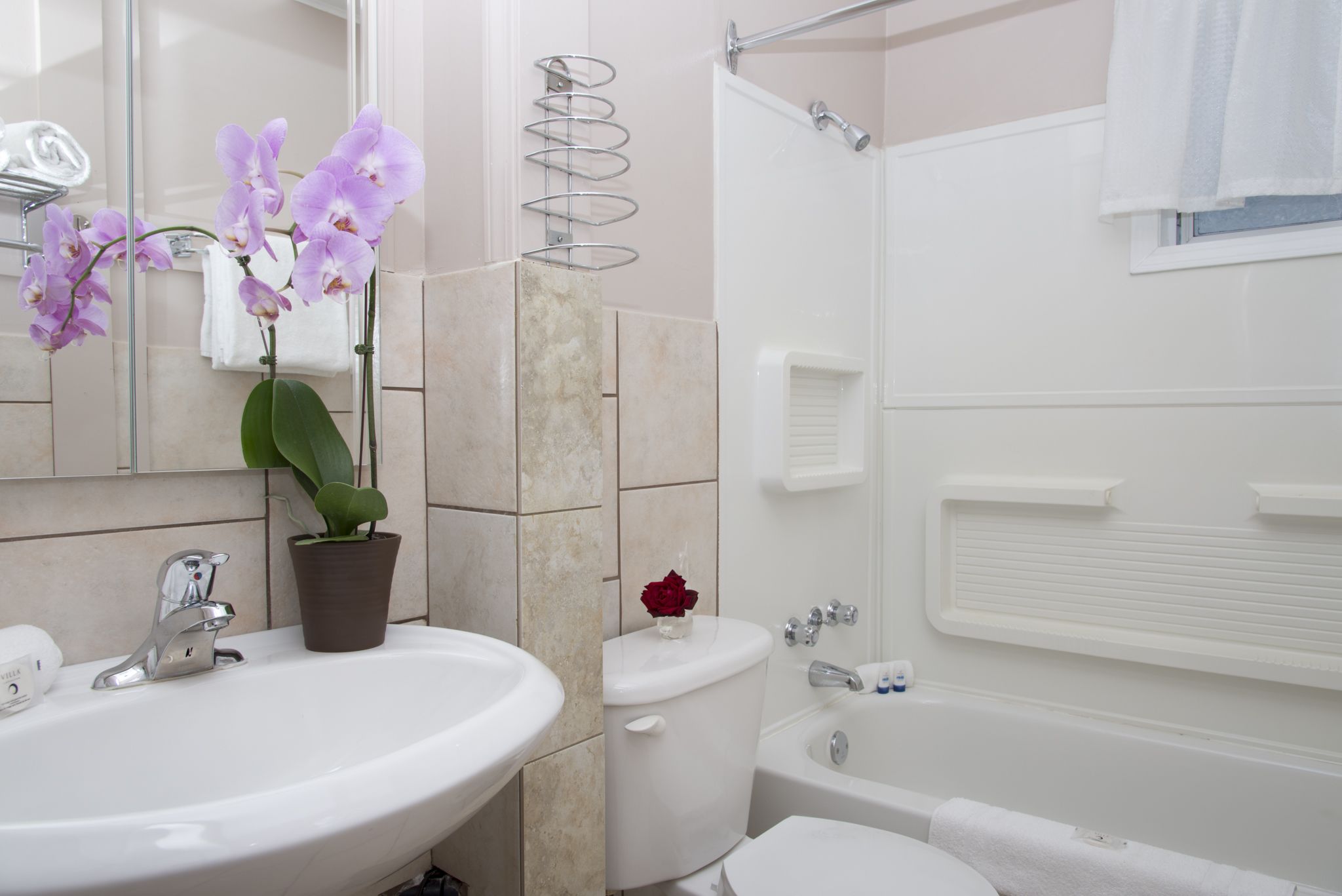 Een badkamer met een wastafel, toilet en badkuip. Er staan orchideeën op de wastafel en een handdoekhouder boven het toilet.