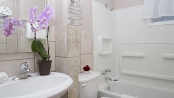 Een badkamer met een wastafel, toilet en badkuip. Er staan orchideeën op de wastafel en een handdoekhouder boven het toilet.