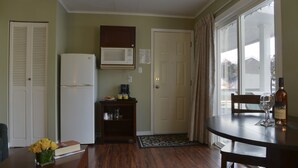 A compact kitchen with a refrigerator, microwave, and a small coffee station. There's a dining table with a wine bottle and glass, and a chair. A door leads to an outdoor area with a view. - Valley Star Motel (Penticton)