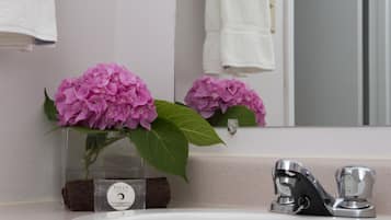 Un baño con un lavamanos blanco, un espejo y un florero de flores rosas.