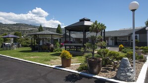 A gazebo with a covered seating area, surrounded by potted plants and a stone feature. - Valley Star Motel (Penticton)